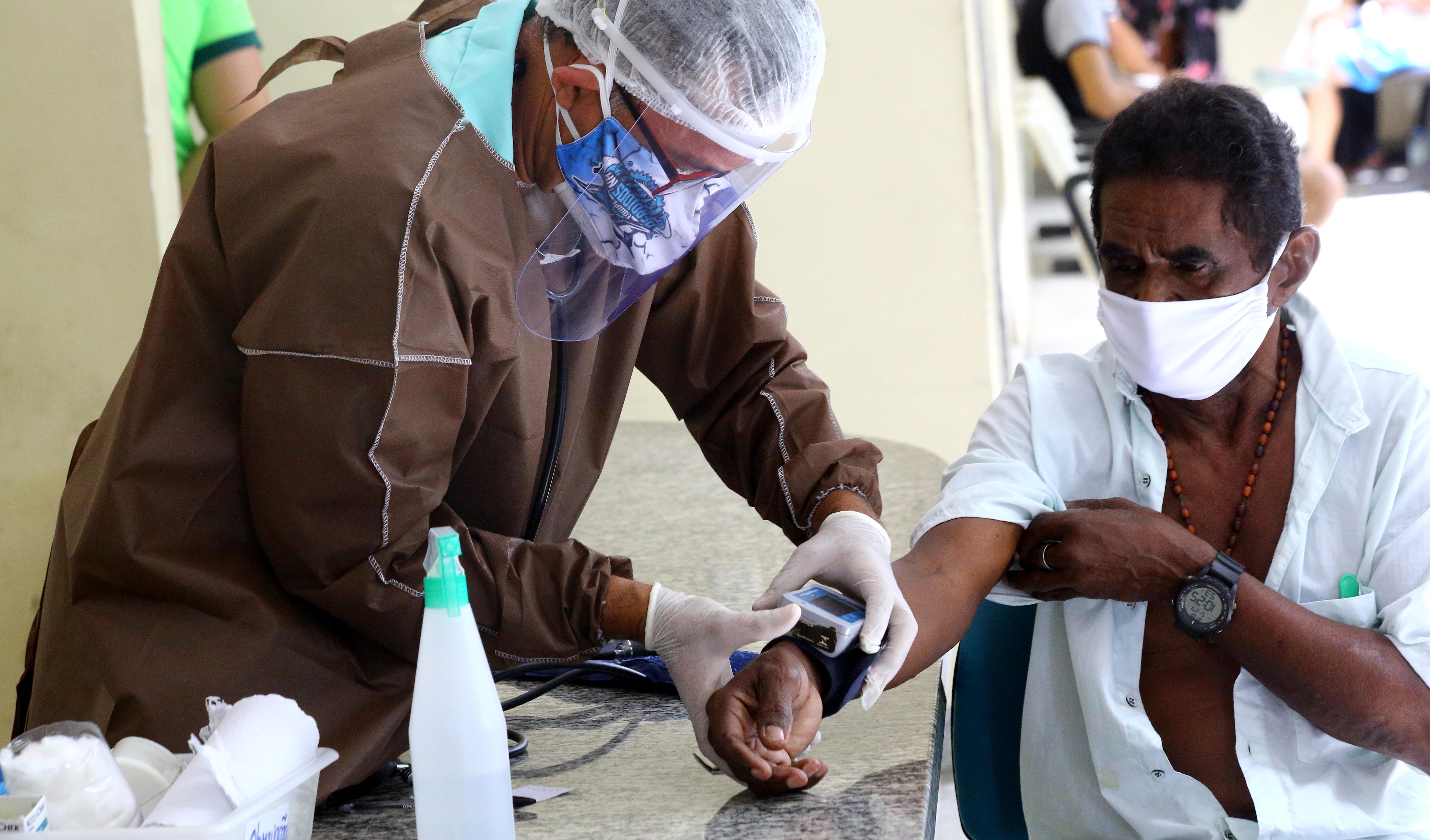 enfermeiro usando EPIs medindo pressão de senhor de máscara em posto de saúde 